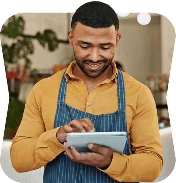 Smiling café owner in a striped apron checking social posts on a tablet behind the counter